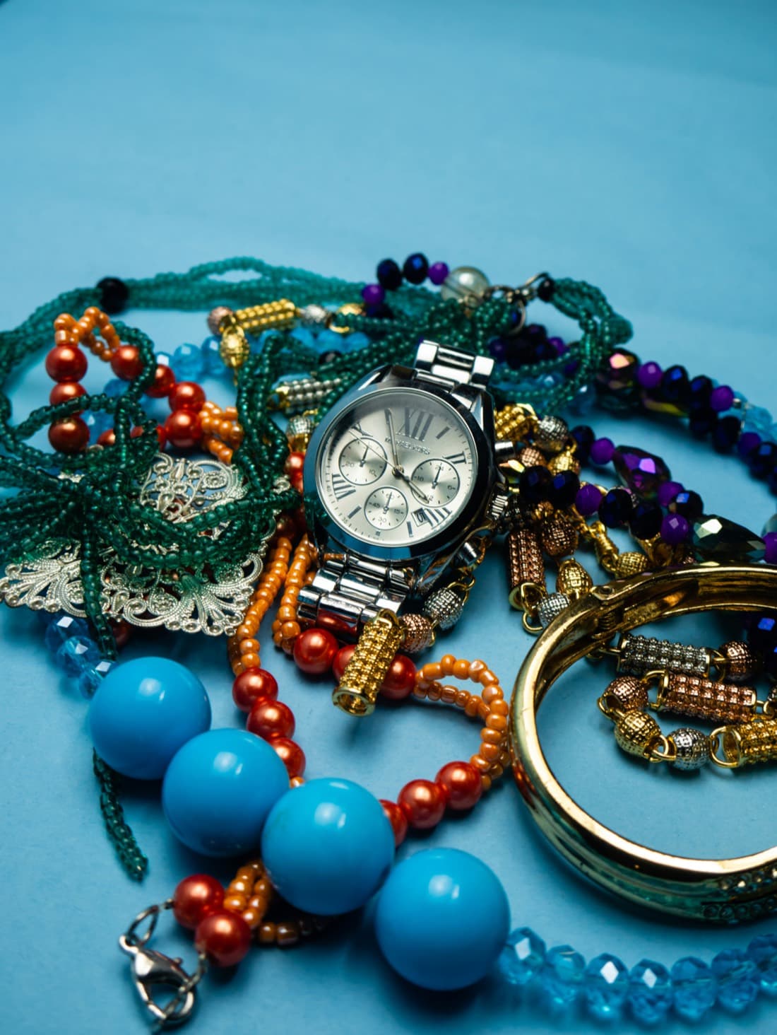 A pile of mixed costume and beaded jewelry with a watch, the way a real collection actually looks