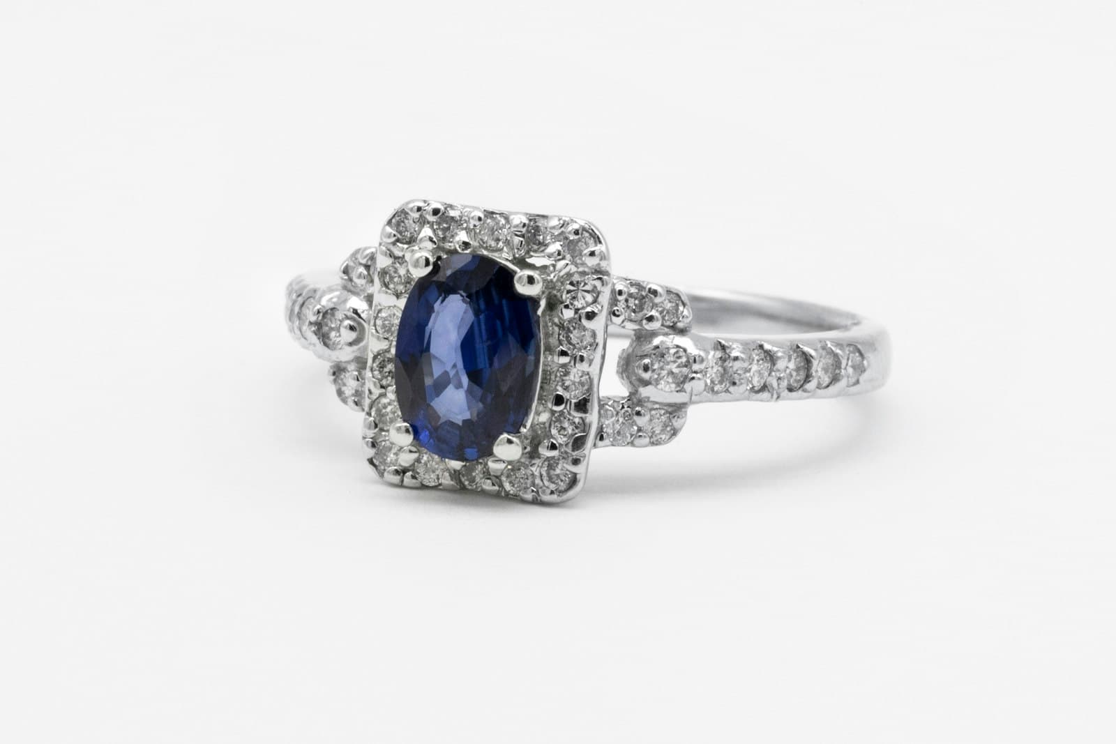 A natural blue sapphire ring with a diamond halo in white gold, photographed on a white background