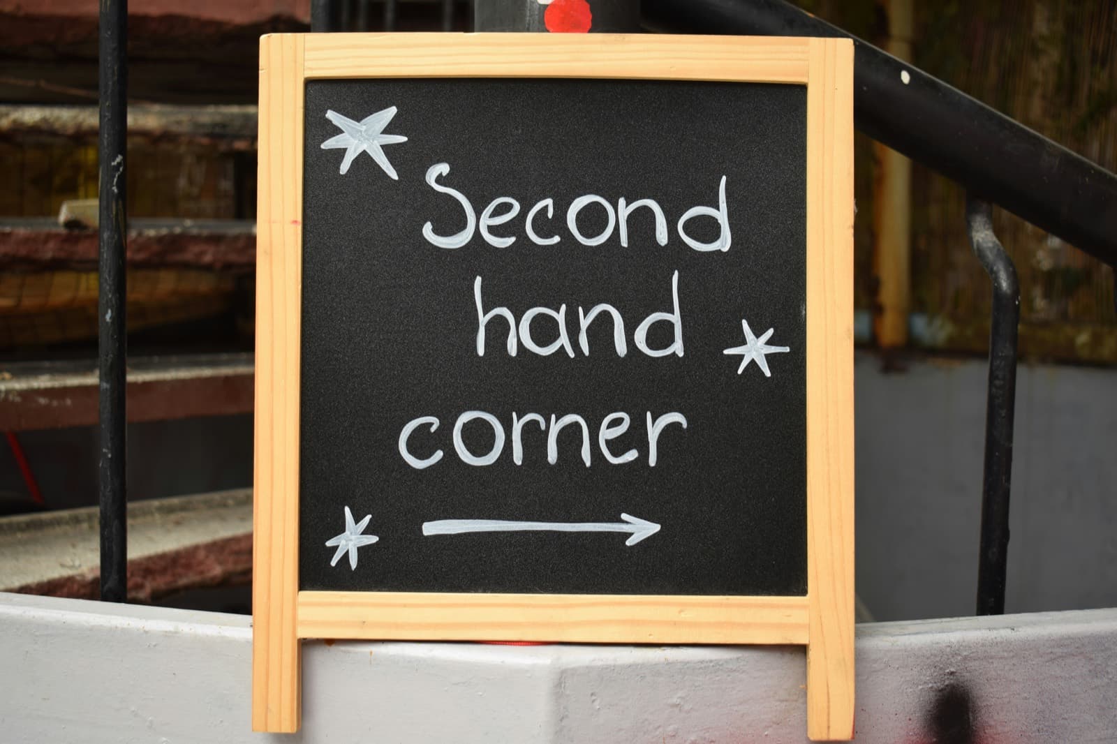 A chalkboard sign reading ‘Second hand corner’ with an arrow, propped on a shopfront step