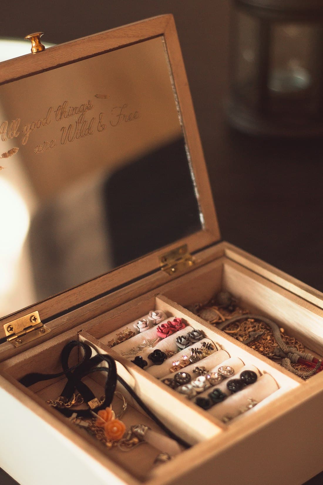 An open wooden jewelry box with rows of stud earrings tucked into velvet rolls