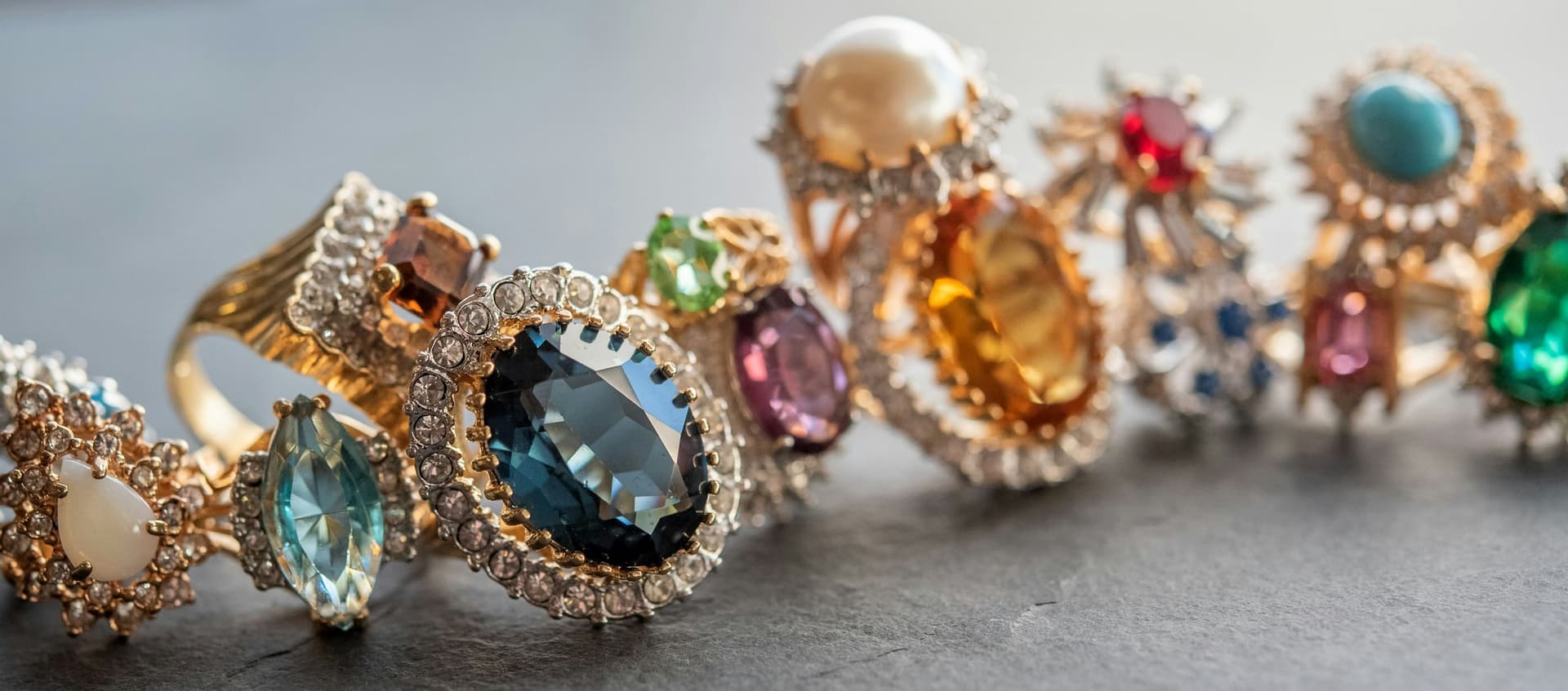A row of colorful vintage cocktail rings with large gemstones lined up on dark slate