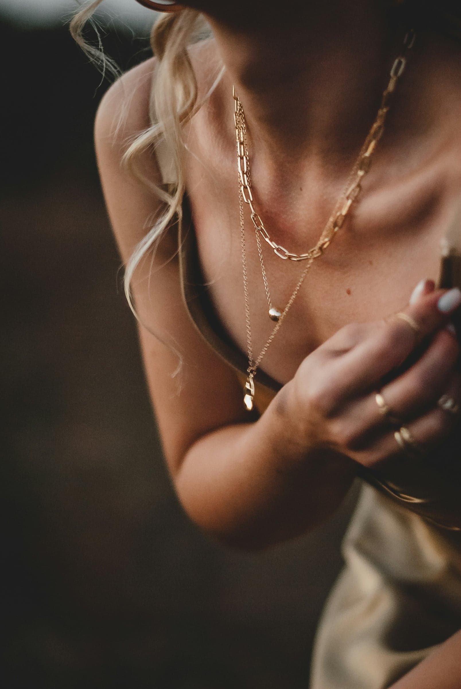 A woman in golden-hour light wearing layered gold chain necklaces and stacked rings